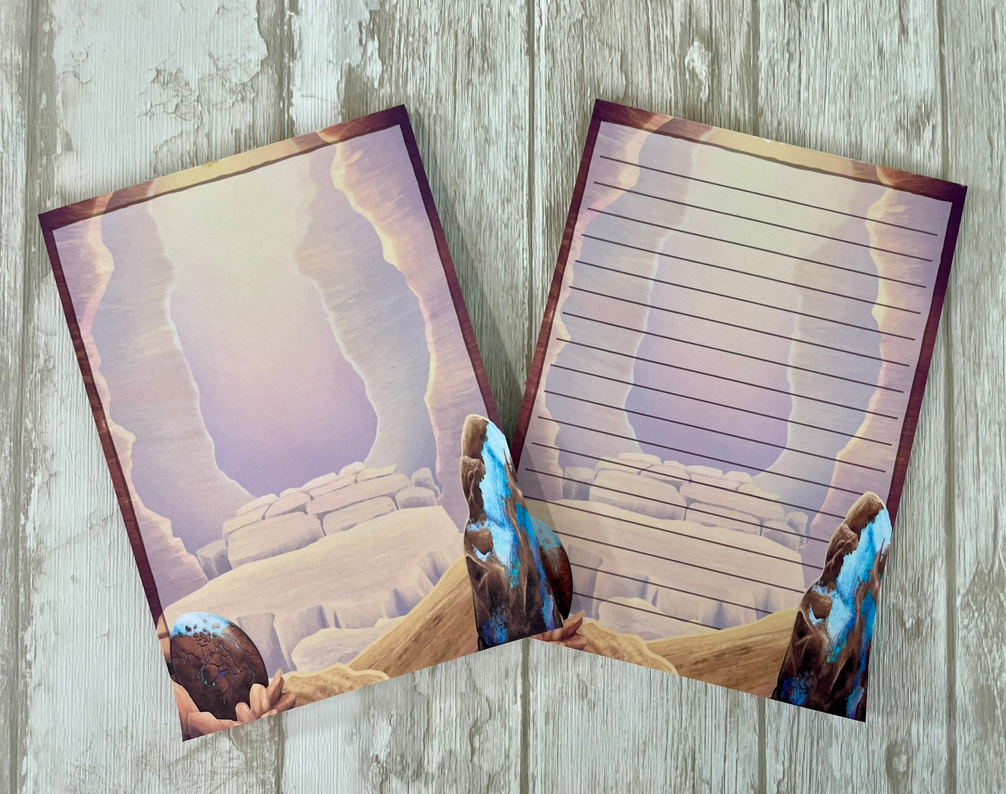 Two 5 by 7 inch notepads with 50 pages that each feature the mesa canyon that is the background from the art print. Each page background show off the opal dragon egg in the left bottom hand corner and a large raw opal mineral rock on the bottom right hand corner. One design is blank and the other has lines to write on.