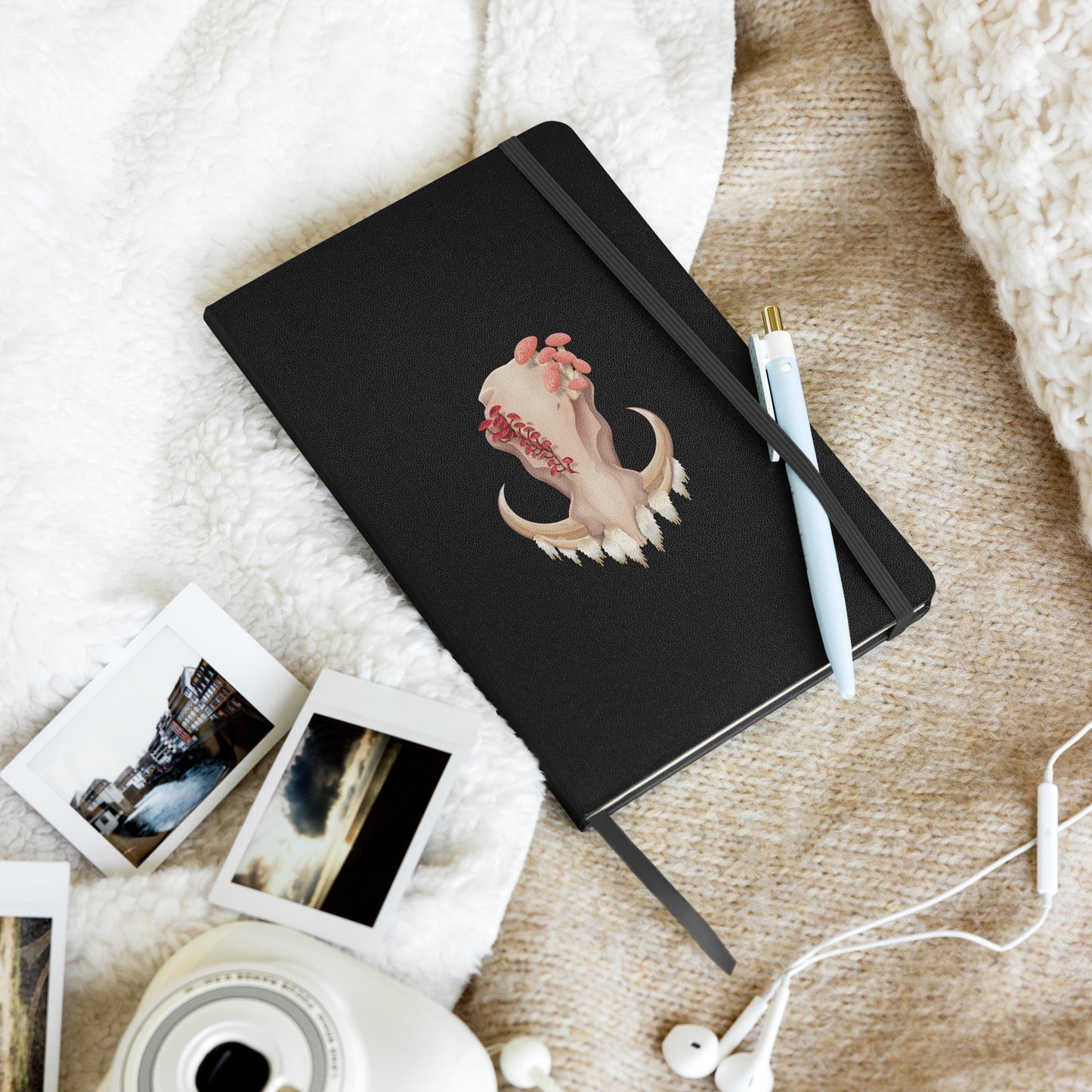 A 80 page, black hardback lined journal with a pocket in the back, a ribbon book mark, and elastic closure, featuring a front facing warthog skull with 3 different kinds of fungi growing out of it