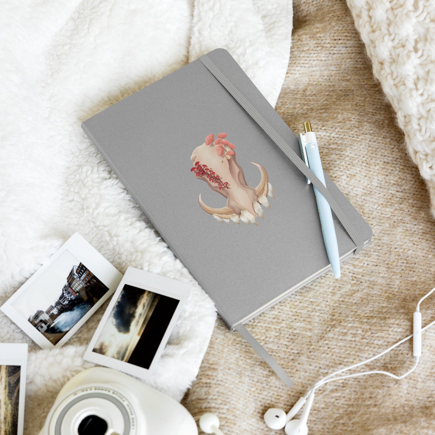 A 80 page, silver hardback lined journal with a pocket in the back, a ribbon book mark, and elastic closure, featuring a front facing warthog skull with 3 different kinds of fungi growing out of it