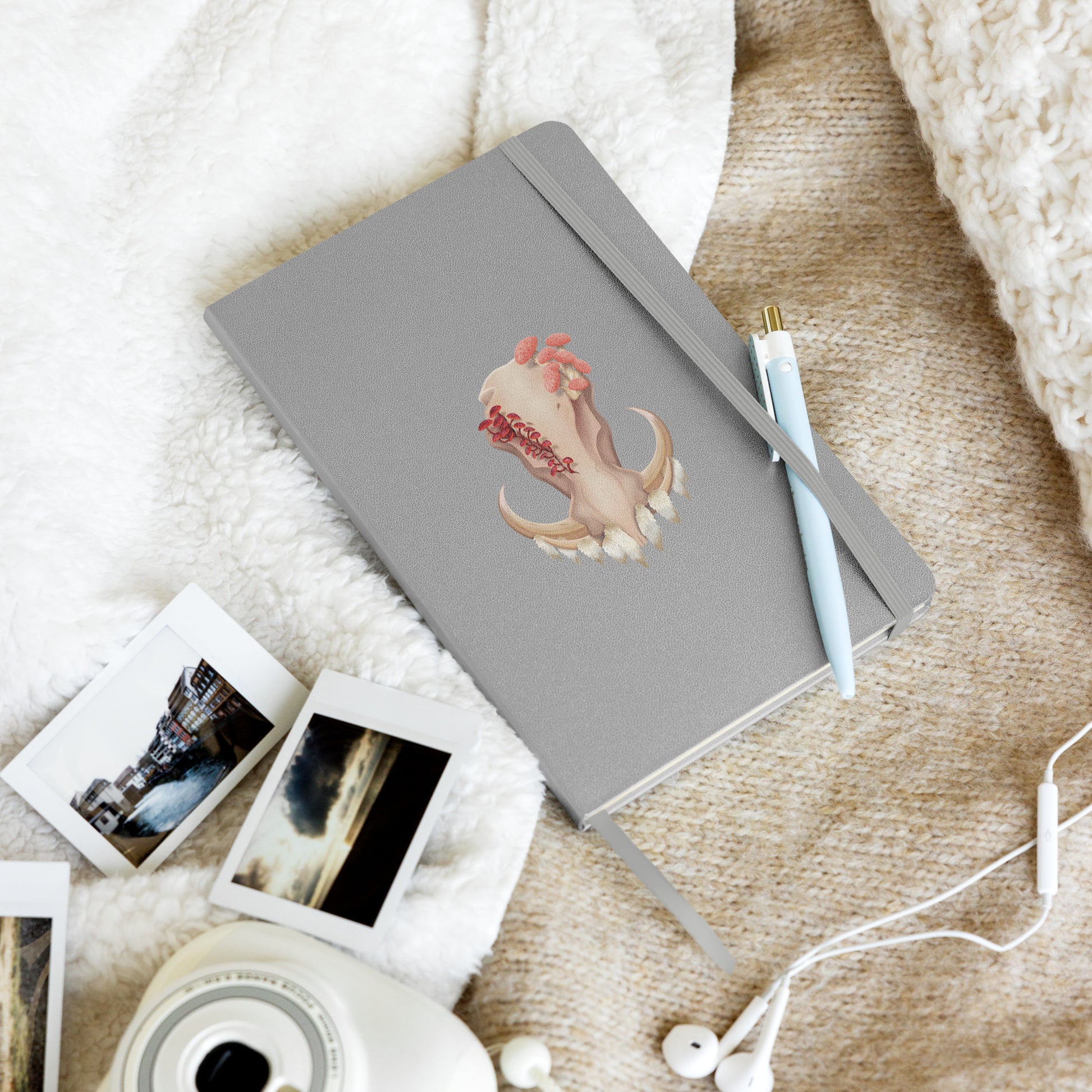 A 80 page, silver hardback lined journal with a pocket in the back, a ribbon book mark, and elastic closure, featuring a front facing warthog skull with 3 different kinds of fungi growing out of it