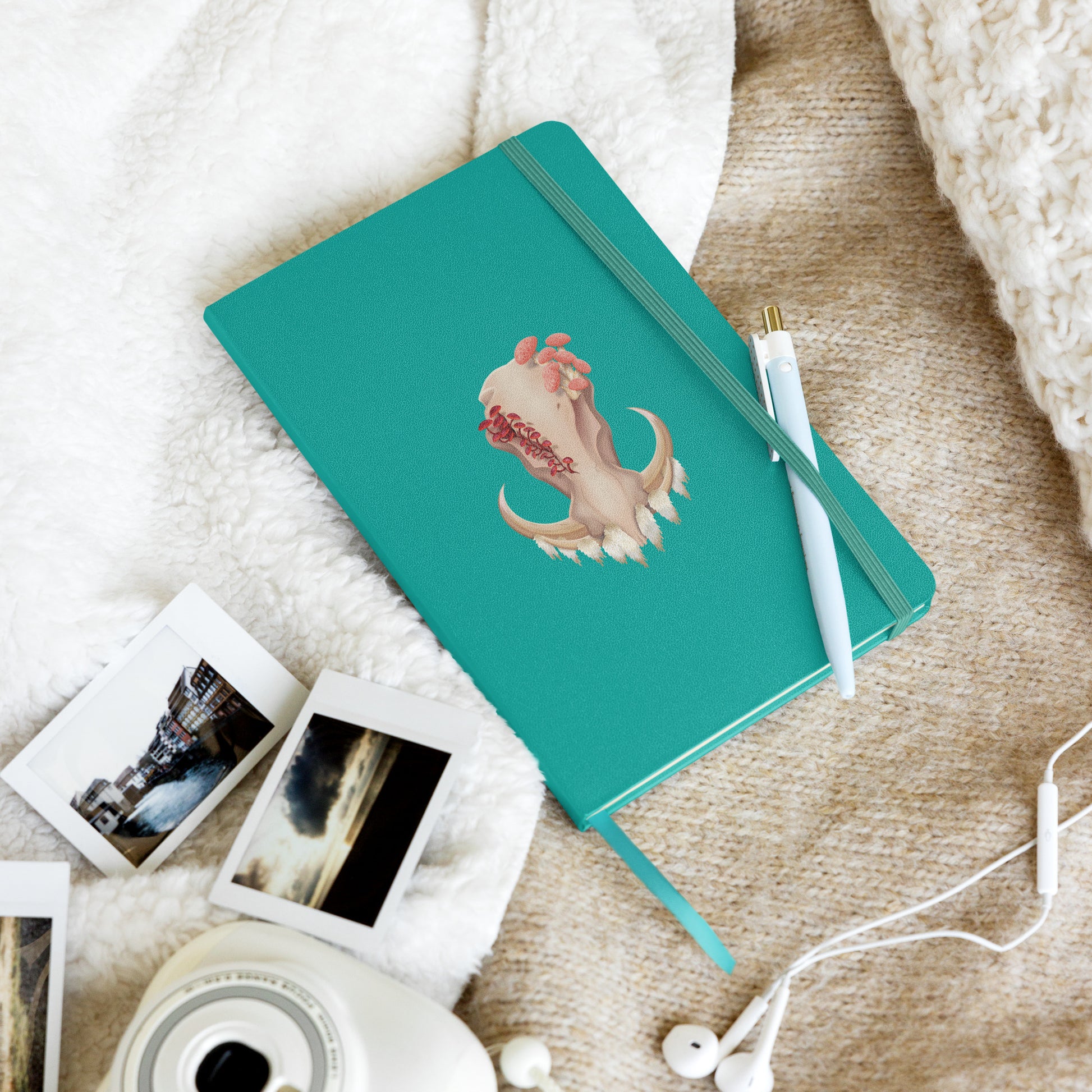 A 80 page, teal hardback lined journal with a pocket in the back, a ribbon book mark, and elastic closure, featuring a front facing warthog skull with 3 different kinds of fungi growing out of it