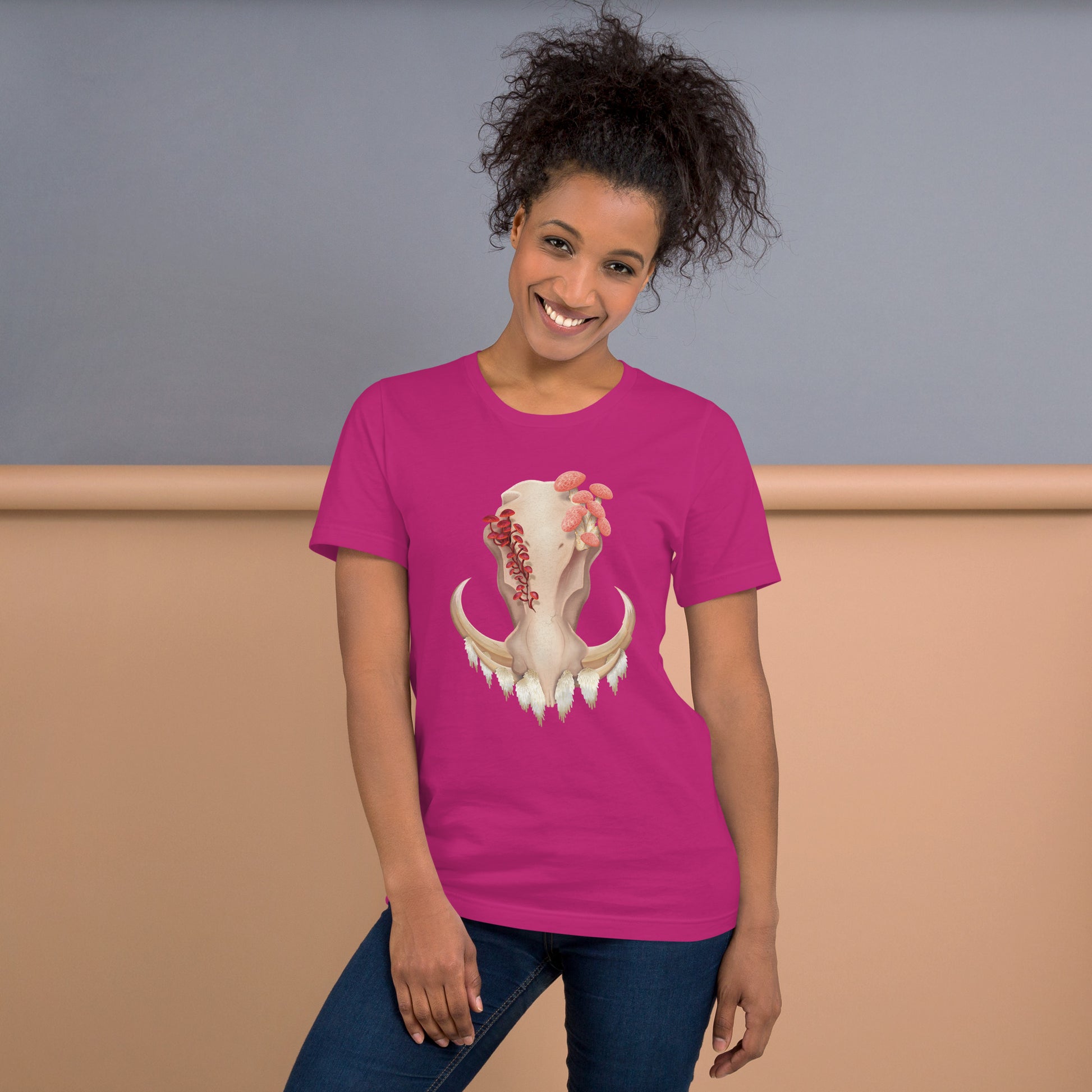 An adult wearing a berry colored, unisex T shirt featuring a front facing warthog skull with 3 different kinds of fungi growing out of it