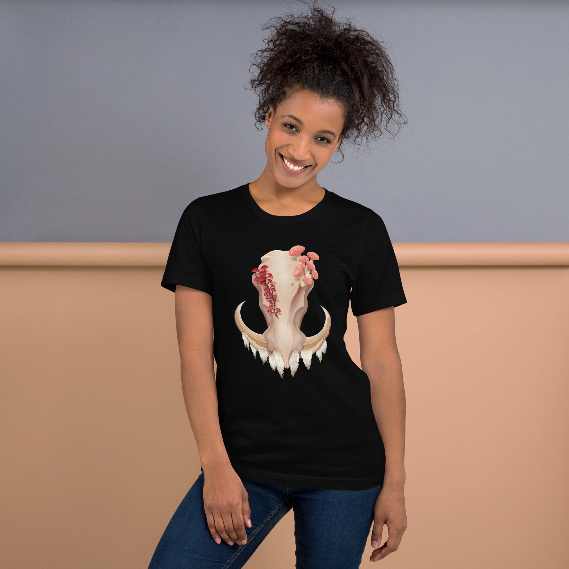 An adult wearing a black colored, unisex T shirt featuring a front facing warthog skull with 3 different kinds of fungi growing out of it