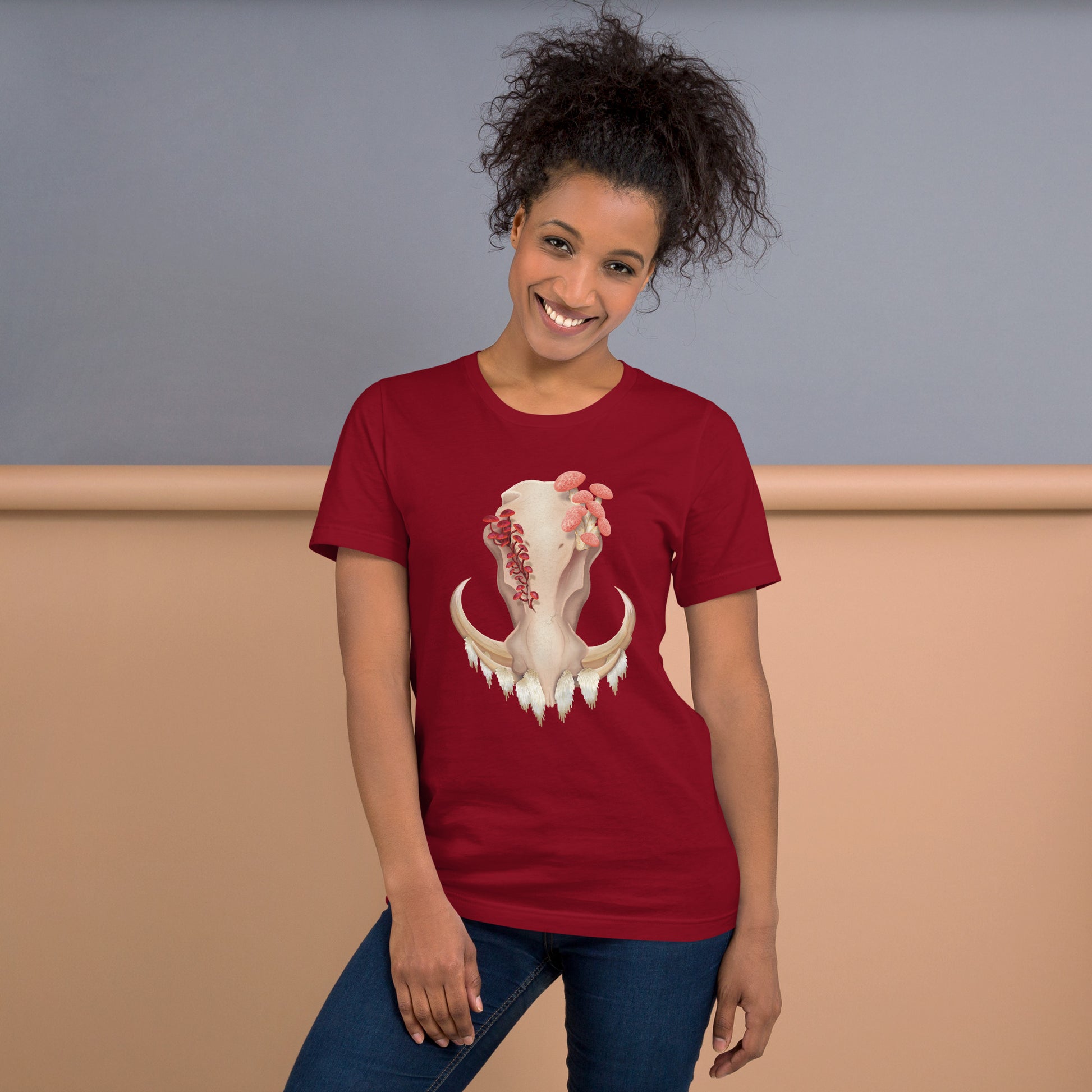 An adult wearing a cardinal colored, unisex T shirt featuring a front facing warthog skull with 3 different kinds of fungi growing out of it
