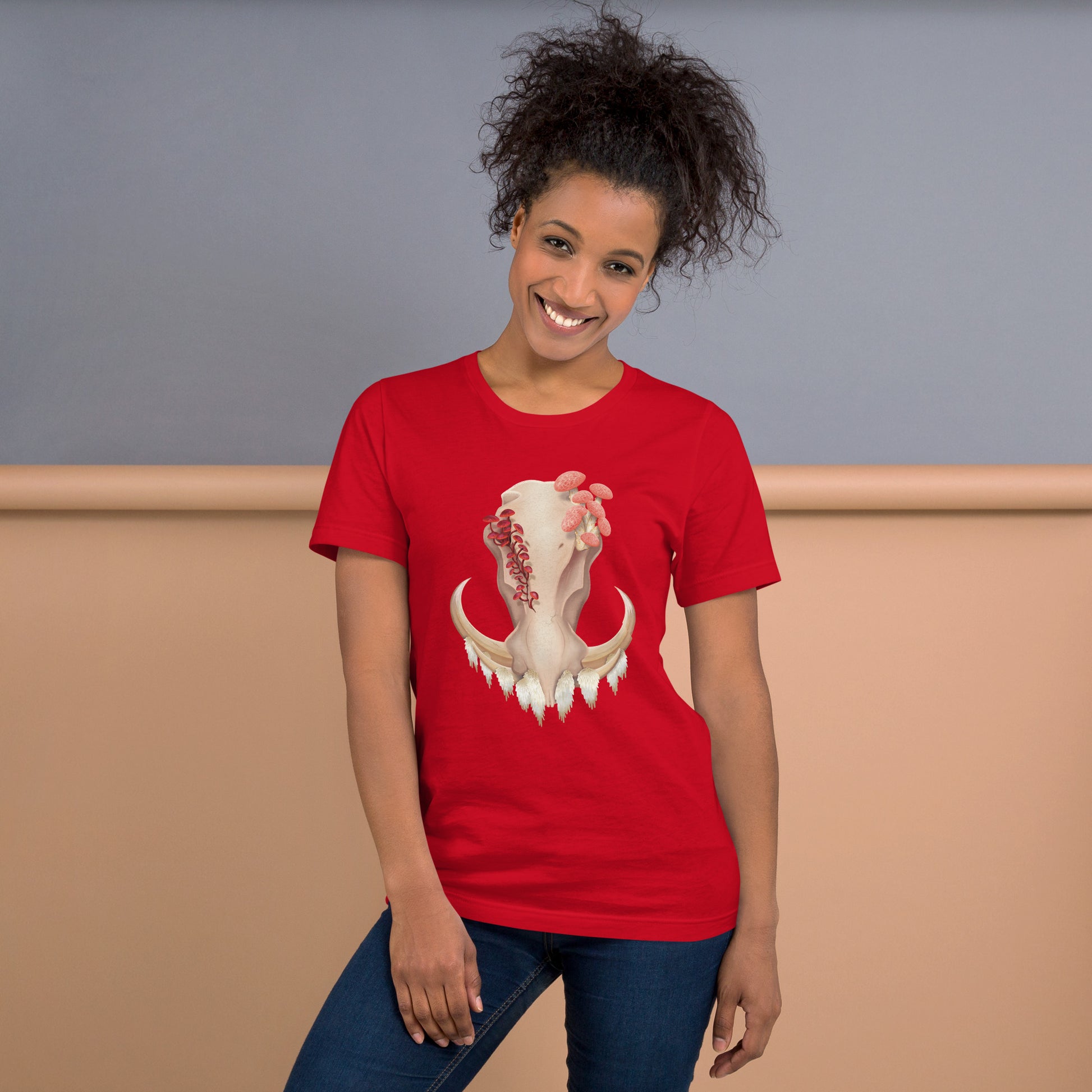 An adult wearing a red colored, unisex T shirt featuring a front facing warthog skull with 3 different kinds of fungi growing out of it