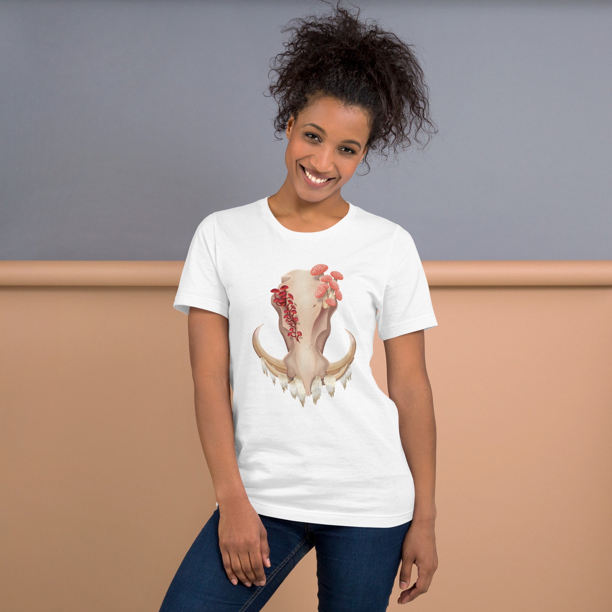 An adult wearing a white colored, unisex T shirt featuring a front facing warthog skull with 3 different kinds of fungi growing out of it